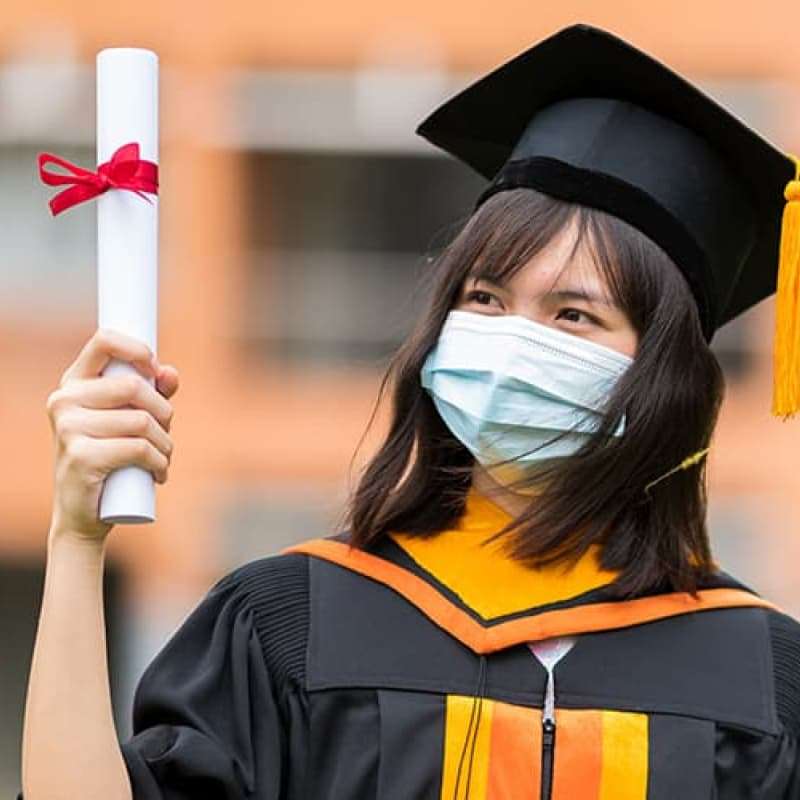 Young woman in face mask in graduation gown, e-Surgery