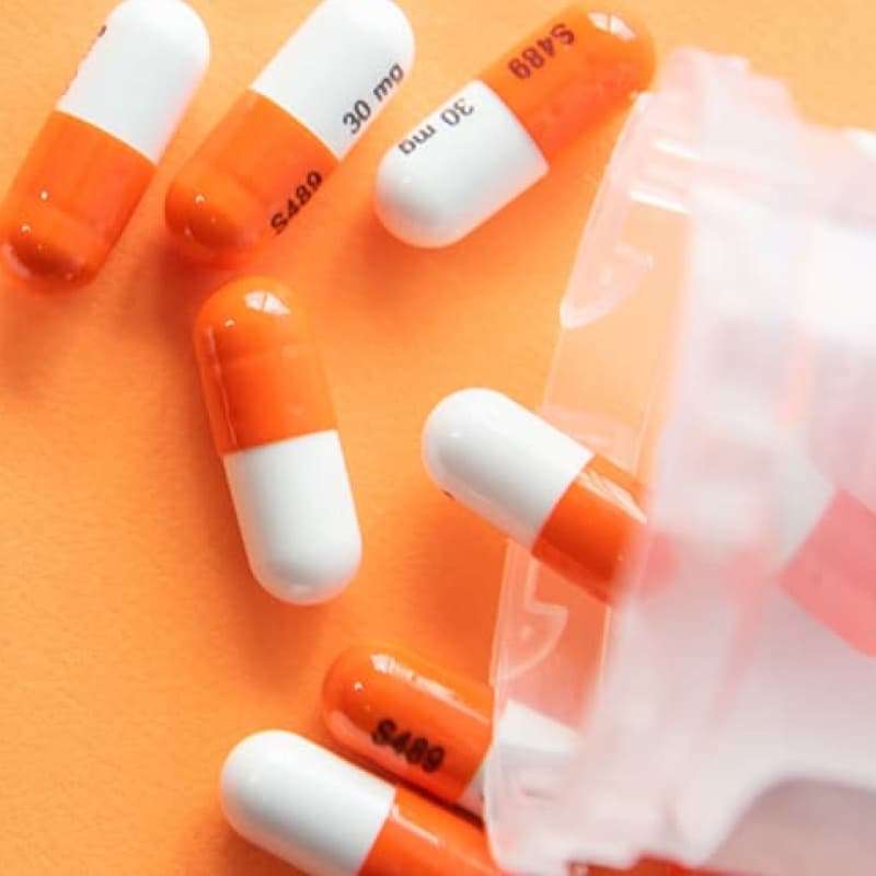 Orange capsule medication pills falling out onto surface from plastic medication pot, how to Avoid Counterfeit Drugs Online, e-Surgery